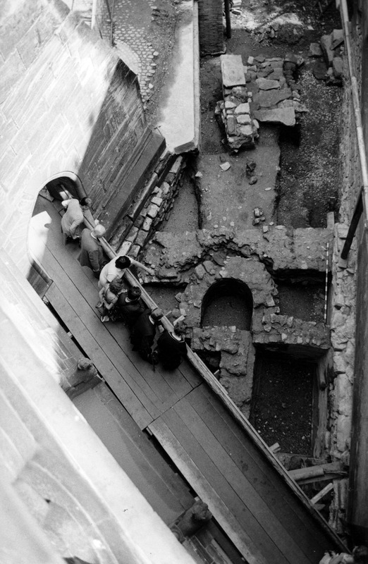 Das Bild zeigt die Grabungsfläche zwischen Niklauskapelle und einem Strebepfeiler des Münsterchors; gut erkennbar ist die Apsis der  Vorkammer der Aussenkrypta, die eine spätrömische Mauer stört. Im Westen wird die Vorkammer  durch einen L-förmigen Mauerrest aus der Zeit des Heinrichsmünsters unbrauchbar gemacht.  Am östlichen Rand liegen Stufen einer Treppe, die im 12./13.Jahrhundert von der Pfalz zum Rhein führte.