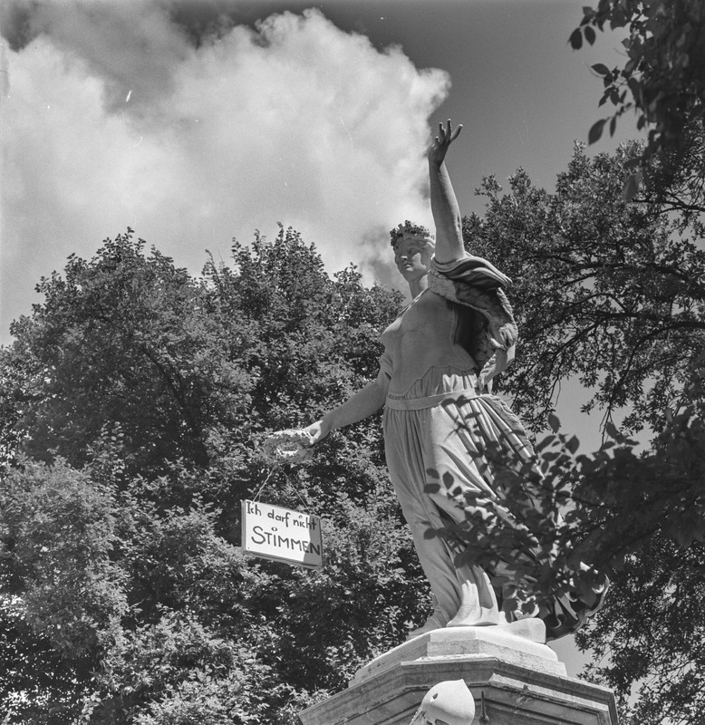 Am 26. Juni 1966 fällten die Basler Männer eine weitreichende Entscheidung: Die Frauen durften von nun an im Kanton wählen, sich für Wahlen aufstellen lassen und abstimmen. Zwei Tage vor der Abstimmung hatten Baslerinnen mit einer symbolhaften Aktion an das bisherige System der Ungleichbehandlung erinnert: «Ich darf nicht stimmen», schrieben sie auf ein Schild und hängten es dem St. Jakobsdenkmal um. Das Denkmal zeigt die Helvetia, eine allegorische Figur, die zwar die Schweiz versinnbildlicht, aber als Frau bis dato von der Demokratie gänzlich ausgeschlossen gewesen wäre – in Basel-Stadt bis 1966, von der nationalen Politik bis 1971, in einzelnen Kantonen sogar noch länger.