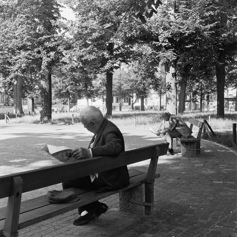 Stadtansicht, Petersplatz: Zwei Männer lesen Zeitung auf Parkbänken.